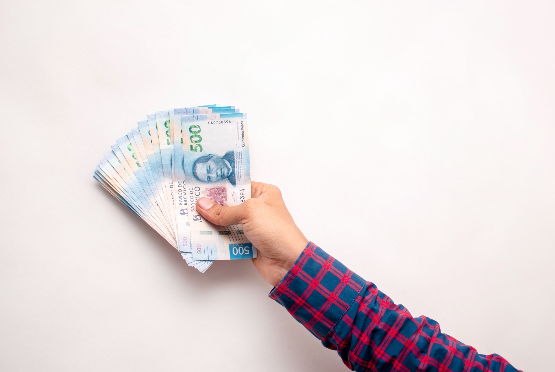 A man's hand holding several Mexican bills on a white background